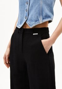 Zwarte linnen broeken met een rechte pasvorm, subtiele textuur en zijzakken. Gecombineerd met een blauwe denim cropped vest met knoopdetails.
