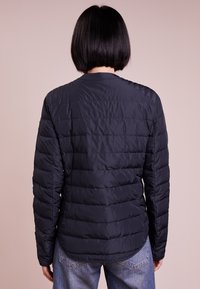Navy puffer jacket with quilted texture, long sleeves, and rounded hem. Features a stand collar and no visible hardware.