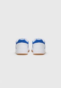 Baskets blanches avec des accents bleus, dos arrondi, semelles en caoutchouc texturé et col rembourré. Présente un design simple et un schéma de couleurs contrasté.