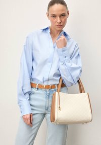 Camisa de manga larga azul claro, vaqueros de mezclilla claros y un bolso blanco con detalles marrones. El bolso tiene un patrón texturizado y asas cortas.