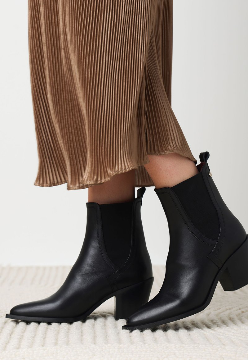 Bottines en cuir noir à bout pointu et talon carré, avec des panneaux élastiques sur les côtés et une languette à l'arrière.