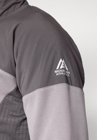 Gray athletic jacket featuring a textured design with a smooth upper portion, and "Mountain Athletics" logo in white on the sleeve.