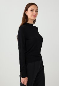 Czarny sweter wykonany na drutach z wysokim kołnierzem, długimi rękawami i złotymi guzikami na mankietach. Dopasowany krój o gładkiej fakturze.