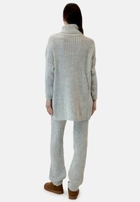 Maglione grigio a coste con collo alto, abbinato a pantaloni coordinati a coste. Tessuto morbido, vestibilità rilassata e maniche lunghe. Calzature marroni.