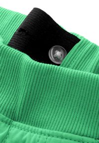 Grön ribbad tyg med ett svart elastiskt band högst upp och en klar plastknappsdetalj, som visar en jämn textur och sömnad.