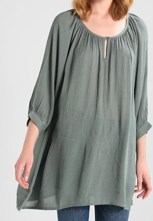 Blouse ample vert clair avec manches 3/4, encolure froncée et détail œillet. Confectionnée en tissu texturé, design fluide.