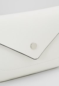 Gros plan sur une pochette blanche en cuir texturé de style enveloppe avec une fermeture à bouton-pression circulaire argentée.