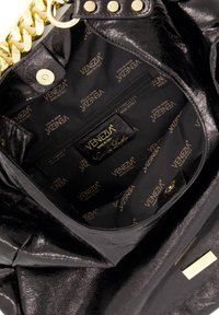 Binnenkant van een zwarte neplederen handtas met een ritszak. De voering is bedrukt met gouden "VENEZIA" branding en heeft een glanzende textuur.