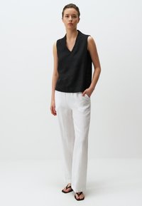 Zwarte mouwloze top met een V-hals, gecombineerd met een witte linnen broek met wijde pijpen en platte zwarte sandalen. Eenvoudige, strakke lijnen en een lichte textuur.