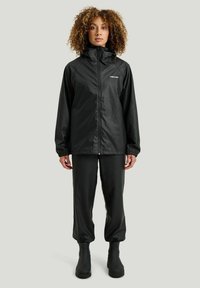 Svart vattentät jacka med hög krage och elastiska muddar. Kombinationen med eleganta svarta byxor och vattentäta stövlar ger en komplett look.