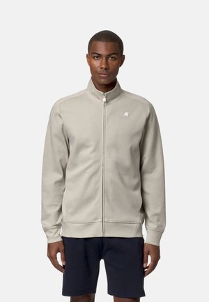 Giacca zip-up grigio chiaro realizzata in tessuto morbido, con colletto alto, polsini a costine e un piccolo logo sul petto.