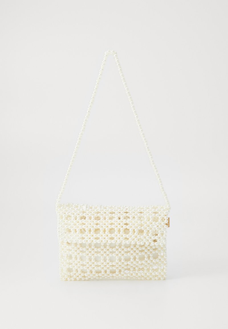 Balta perlų puošmenomis dekoruota rankinė su struktūrizuotu dizainu, išsiskirianti grandine rankena ir ertmėmis, sukurtomis perlų.
