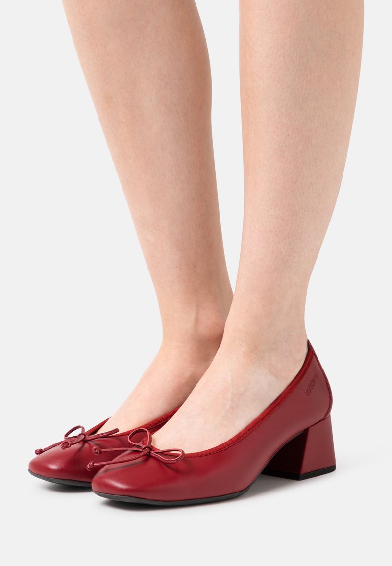 Chaussures en cuir rouge à talons carrés, avec un bout arrondi, ornées d'un nœud décoratif sur le cou-de-pied et une surface texturée.