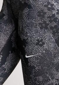 Czarne legginsy z kropeczkowym wzorem w odcieniach szarości. Zawierają małe białe logo Nike w dolnej części. Gładka faktura.