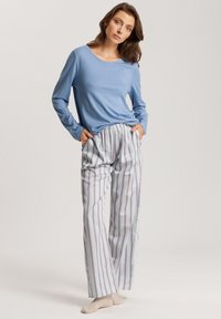 Top de manga larga azul claro combinado con pantalones de pijama sueltos a rayas en tonos de blanco, púrpura y azul. Tela suave, cinturilla elástica.