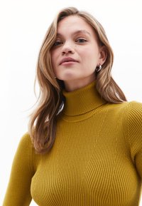 Sweter z wysokim kołnierzem w kolorze musztardowym, prążkowany, z pionowym wzorem. Gładka faktura, dopasowany krój.