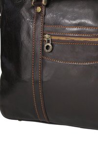 Dark brown leather bag with a smooth texture, featuring a zippered pocket and accented stitching in lighter brown. Brass hardware detail visible.