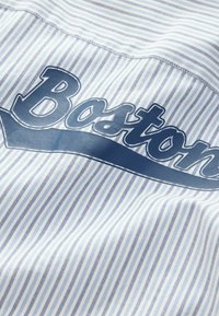 Csíkos anyagú ing világoskék és fehér színben. Elöl egy feltűnő, sötétkék "Boston" grafika található. Simogató tapintású, klasszikus gallérral rendelkezik.
