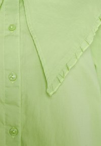 Camisa de algodão verde-claro com fecho de botão, borda da gola com pregas e textura suave com detalhes de costura discretos.