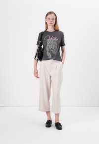 Grijze t-shirt met luipaardprint en "Wild" tekst in roze, gecombineerd met lichtbeige wijde broek en zwarte instap schoenen. Zwarte tas inbegrepen.