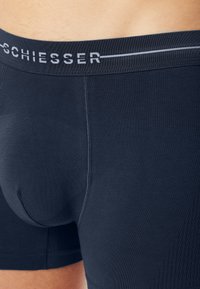 Närbild av en person som bär mörkblå Schiesser kalsonger med en synlig elastisk midjeband och en formad framficka.