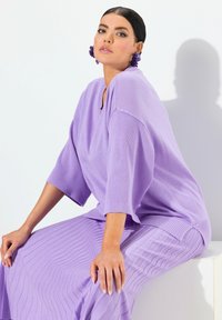 Maglione lavorato a maglia di colore viola chiaro, con vestibilità over e maniche a costine, abbinato a una gonna testurizzata coordinata con motivi a onda.