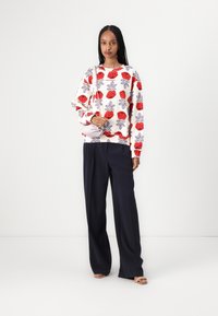 Sweatshirt with red and purple floral pattern on white fabric, paired with navy wide-leg trousers; model holds a small light purple bag.