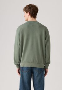 Groene sweatshirt met lange mouwen, een ronde hals en geribbelde manchetten en zoom. G gedragen met blauwe denim jeans met achterzakken.