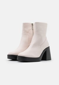 White leather ankle boots with a high, ribbed black heel and side zipper. Smooth texture and rounded toe design.