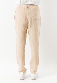 Beige linnen broek met elastische tailleband, rechte pijpen en zijzakken. Heeft een klein roze logo-label op de achterzijde van de taille.