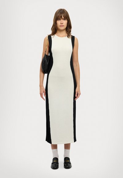 Abito senza maniche in bianco e nero con un design aderente, pannelli laterali a contrasto e taglio al ginocchio; abbinato a una borsa nera e mocassini.