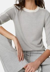Suéter gris de punto con un cuello acanalado y acentos en un gris claro en los hombros. Combinado con pantalones gris a juego, que muestran una tela texturizada.