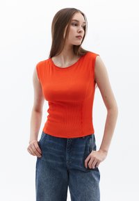 Top arancione a costine senza maniche con scollatura rotonda e silhouette aderente, abbinato a jeans in denim blu a vita alta.