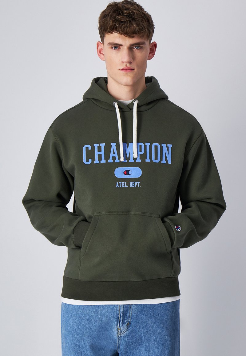 Felpa verde realizzata in materiale morbido con tasca a kangaroo. Presenta un logo blu "CHAMPION" e lacci bianchi. Vestibilità comoda.