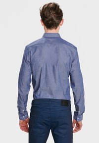 Camisa de manga larga azul claro con cuello y textura sutil. Combinada con jeans azul oscuro y con puños abotonados.