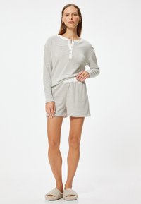 Striped pyjamasæt med langærmet top med knapper og strikkede shorts. Farverne er lyse og neutrale med en blød, hyggelig tekstur.