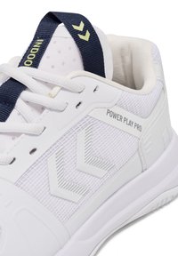 Baskets blanches avec une tige en maille texturée, présentant des accents en zigzag gris et une languette bleu marine avec un logo vert.