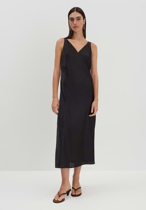 Black midi dress with a V-neckline, made of smooth fabric, featuring a subtle pattern. Worn with brown heeled flip-flops. Minimalist design.