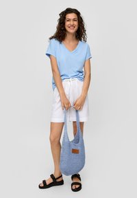  Lichtblauwe v-hals t-shirt, witte linnen shorts met een strik taille, en een blauwe gevlochten tas. Model draagt zwarte sandalen met een gestructureerde band.