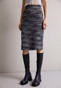 Černobílá pruhovaná tužková sukně vyrobená z elastického materiálu, s hladkým povrchem a slim fit siluetou, doplněná o vysoké černé boty.