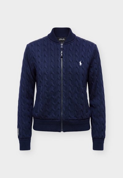 Pull zippé bleu marine en maille torsadée avec col, poignets et ourlet côtelés, avec un petit logo blanc de joueur de polo sur la poitrine gauche.