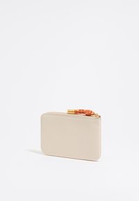Beige leather wallet with a textured finish, zip closure, and orange decorative cord accent. Compact rectangular shape.