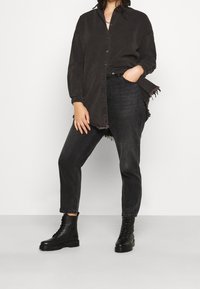 Camisa negra de gran tamaño con cierre de botones, con dobladillo deshilachado, combinada con vaqueros negros de cintura alta y botas de combate negras con cordones.
