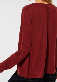 Suéter de punto rojo con un corte holgado, que presenta acentos acanalados en las mangas y los laterales, y un discreto detalle de costura en la parte posterior. Textura suave.