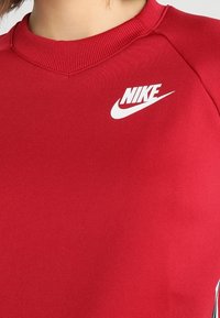 Röd Nike sweatshirts med ribbad krage, med en vit logotyp på bröstet. Slät textur med en avslappnad passform och raglanärmar.