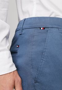 Pantaloni texturizzati azzurro chiaro con vestibilità slim, dotati di un accento logo rosso, bianco e nero vicino all'orlo della vita e una tasca posteriore.
