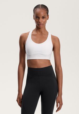 Witte sportbeha met een ronde halslijn, brede banden en een soepele textuur. Gecombineerd met hoge zwarte leggings met naden.