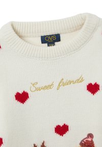 Cremig gestrickter Pullover mit roten Herzmustern, goldfarbenem, gesticktem Text "Süße Freunde" und einem strukturierten Design mit einer bunten Cupcake-Grafik.