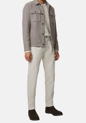 Giacca grigio in misto lana con due tasche sul petto, maglione crema testurizzato, pantaloni bianco sporco e stivali alla caviglia in suede marrone scuro.