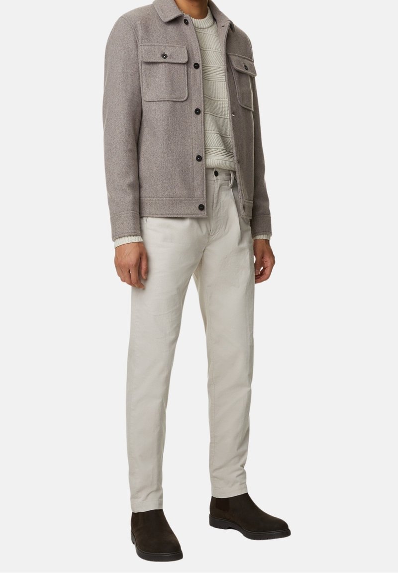 Grå uldblandingsjakke med to brystlommer, cremefarvet struktureret sweater, off-white bukser og mørkebrun ruskinds ankelstøvler.